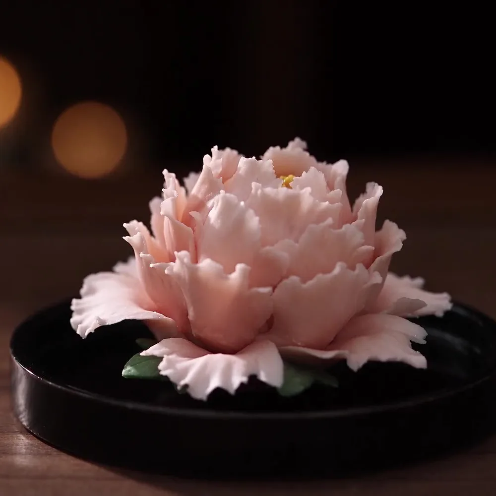 A porcelain peony on a dark wooden counter in warm light